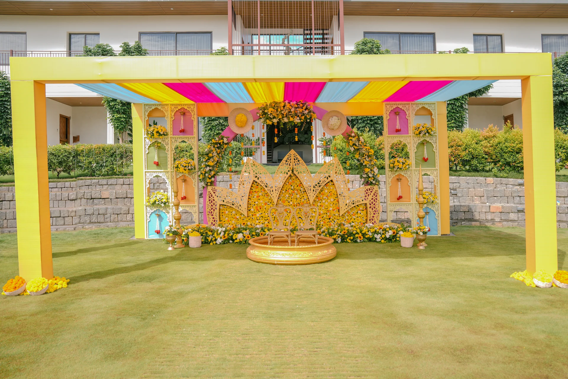 Frontal view of Haldi stage featuring a lotus-inspired floral backdrop, ornate panels and colourful canopy