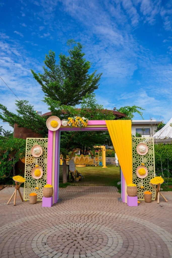Colourful Haldi ceremony entrance with pink and yellow gateway, floral baskets and patterned panels