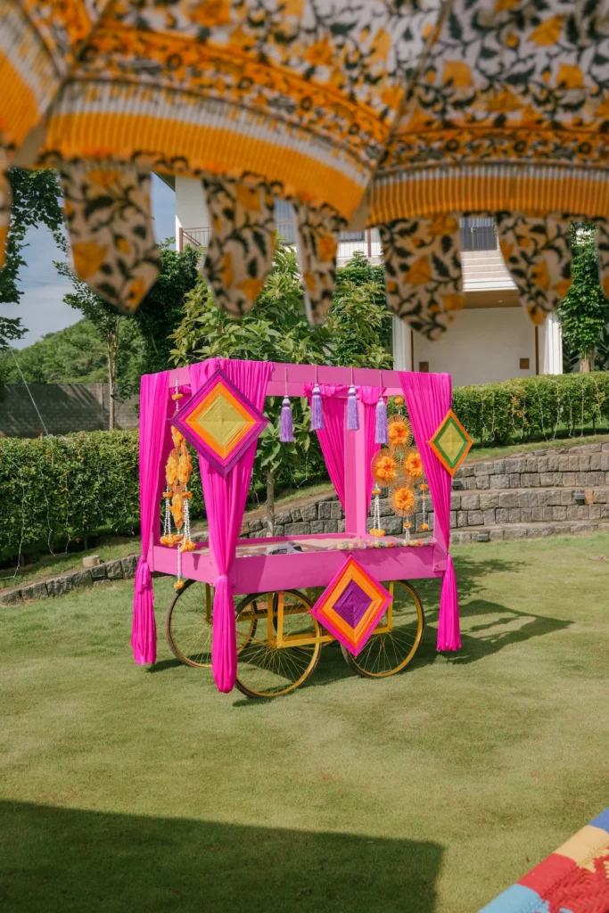 Colourful Haldi ceremony decor cart with pink fabric, marigold flowers and traditional Indian patterns