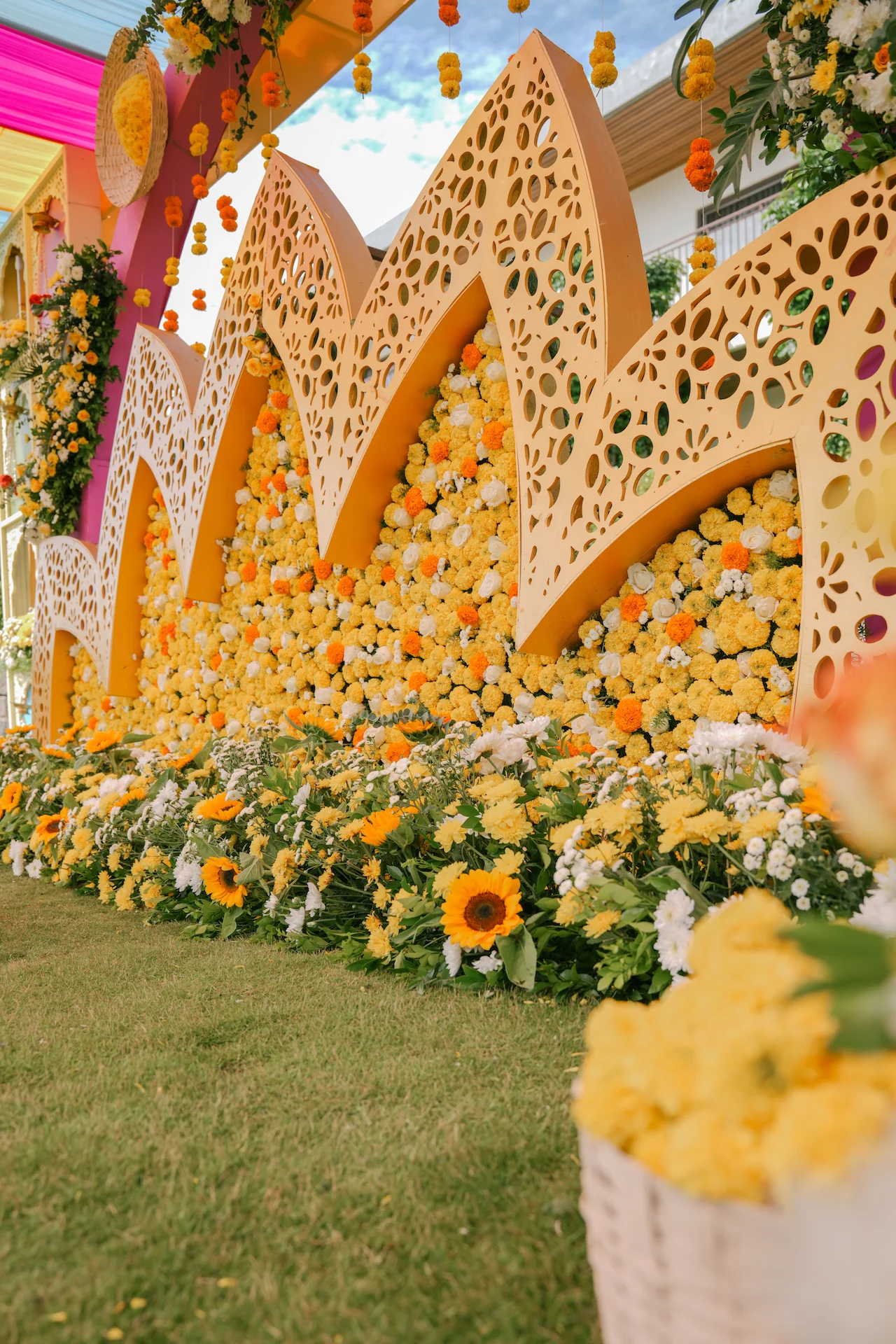 Lotus-inspired Haldi stage backdrop covered in yellow and white marigold flowers with intricate cutwork panels
